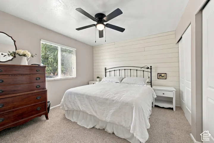 Carpeted room featuring a ceiling fan with integrated lighting, a window with blinds, and a shiplap accent wall