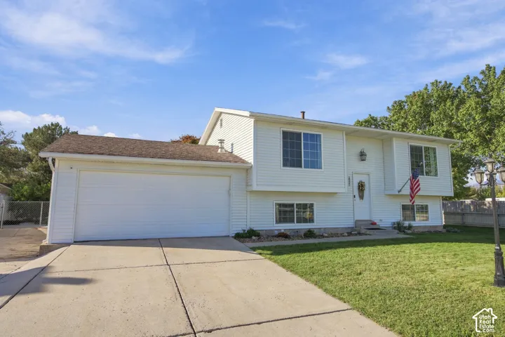 Split-level home featuring white siding, a two-car garage, and a concrete driveway