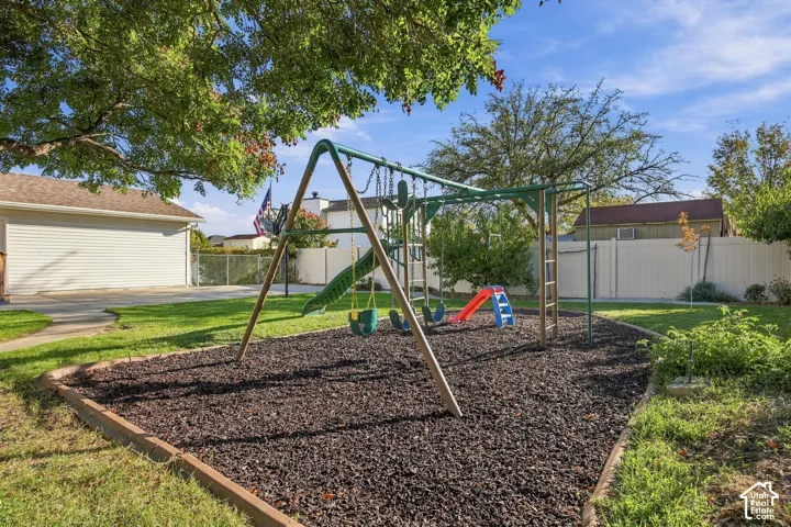 Expansive backyard featuring a swing set with slide, rubber mulch surfacing, manicured lawn, and mature trees