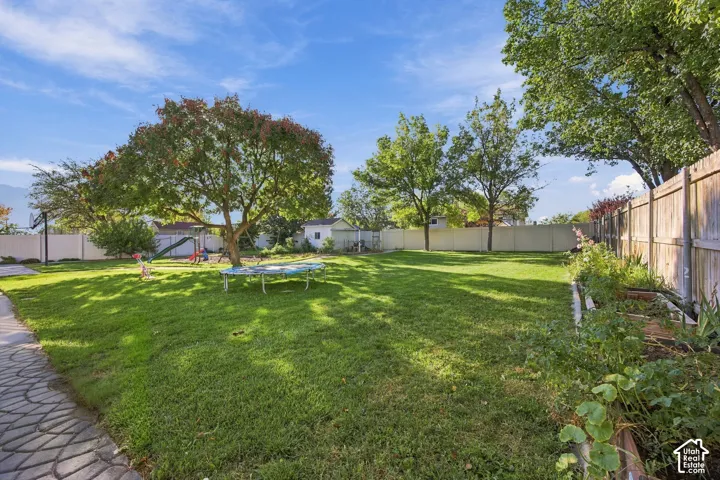 Expansive lawn area with mature trees, a paver pathway, raised garden beds, and a perimeter fence