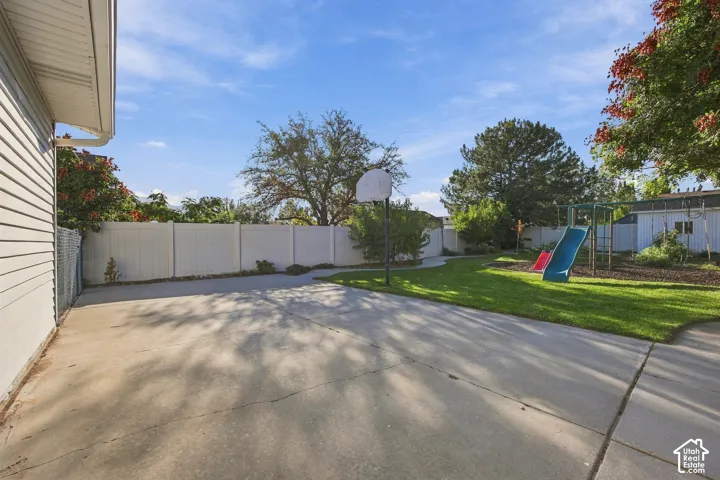Expansive concrete patio with a basketball hoop, surrounded by a white privacy fence