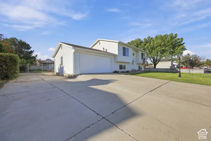 Expansive concrete driveway, attached garage, white siding exterior, mature trees, and a front lawn