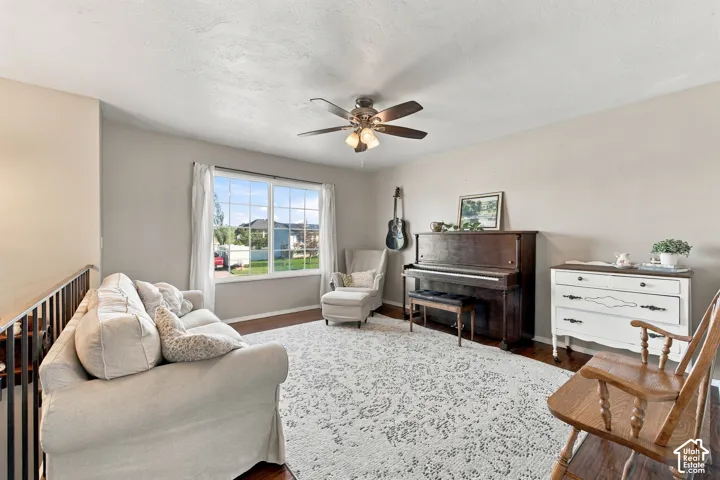 Hardwood-style flooring, ceiling fan with integrated lighting, large window with white trim, light gray wall paint, and white textured ceiling