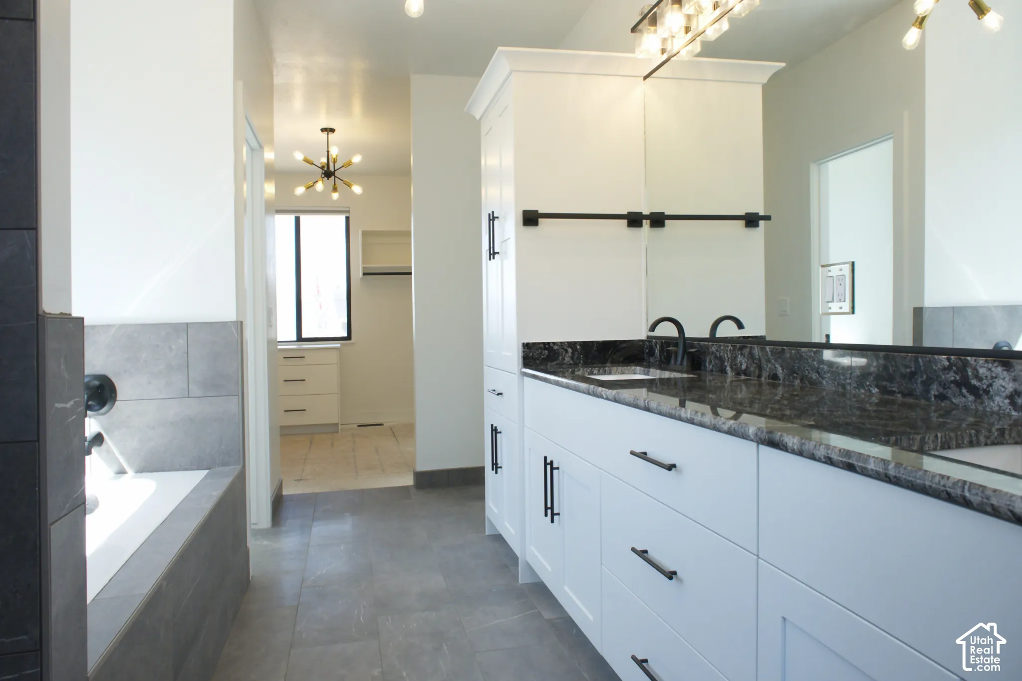 Spa-inspired primary bathroom featuring a freestanding soaking tub with tile surround, dual-sink vanity with dark stone countertops, matte black hardware, and a walk-in shower enclosed in frameless glass