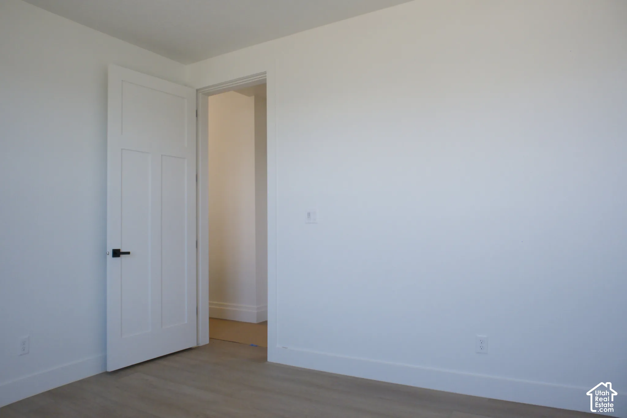 Wood-finish flooring, white walls, and a modern paneled door with matte black hardware