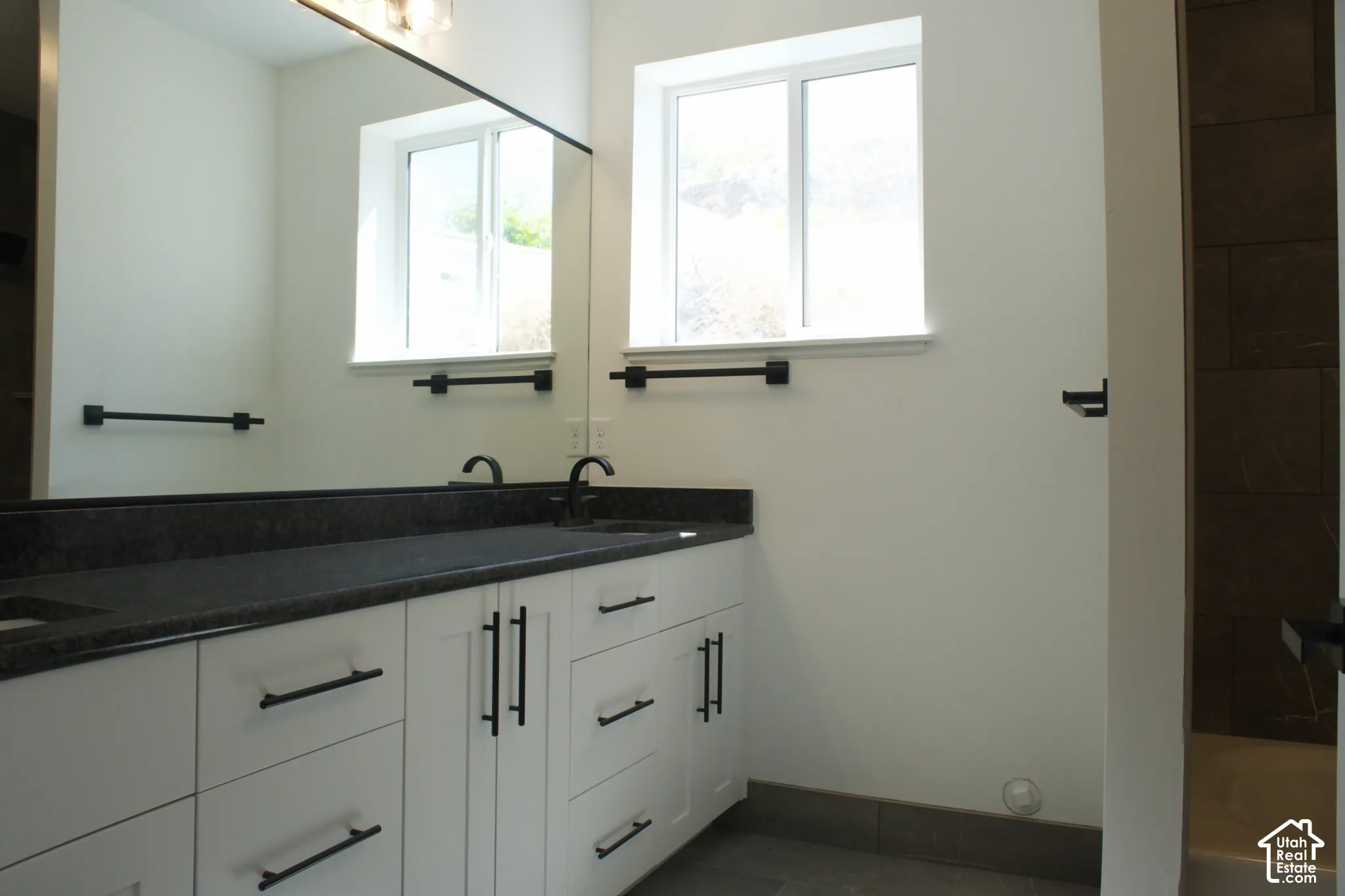 Dual white vanity with dark hardware, dark countertop, and integrated sinks