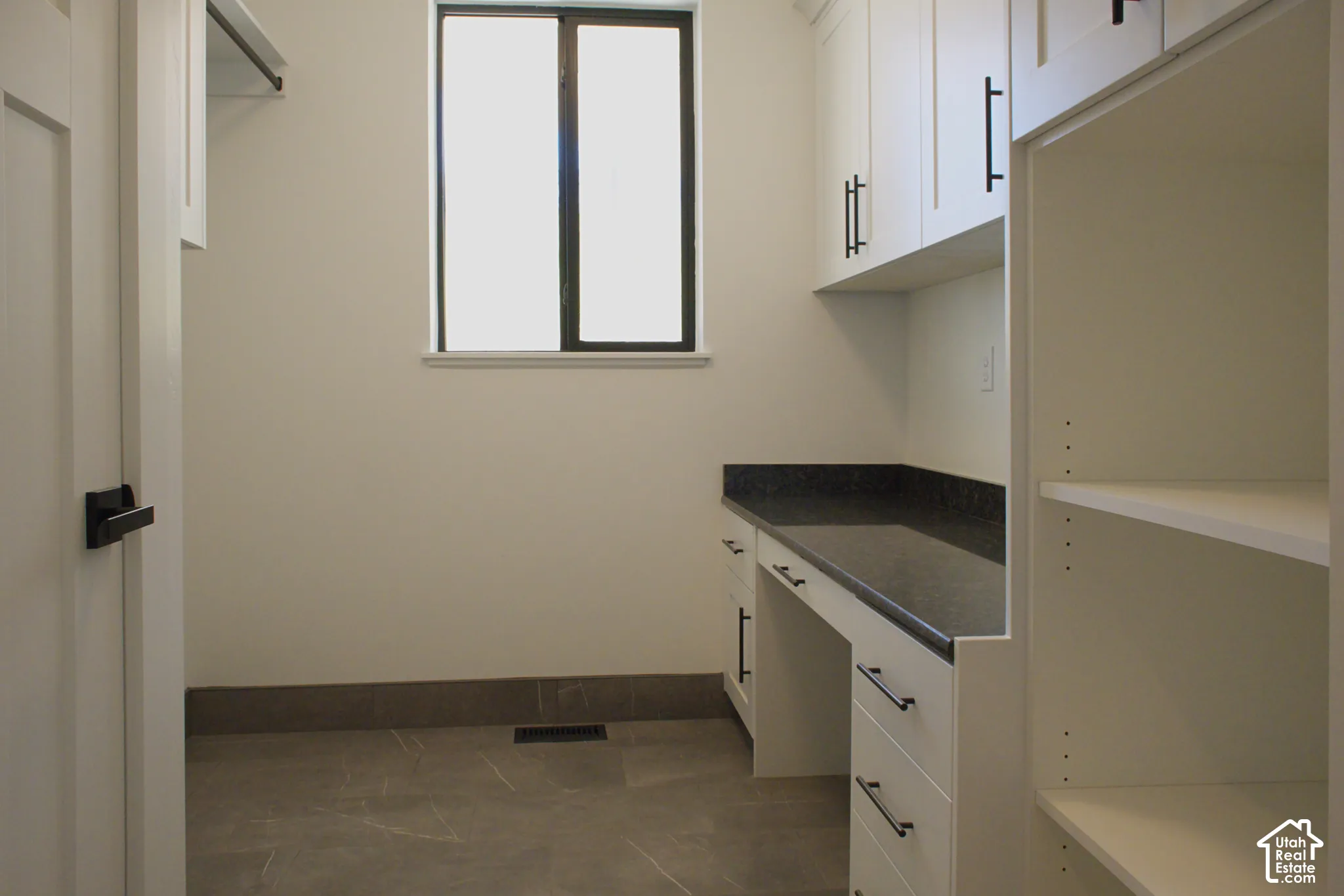 Built-in cabinetry with dark pulls, dark countertop, window for natural light, tile flooring, and integrated shelving
