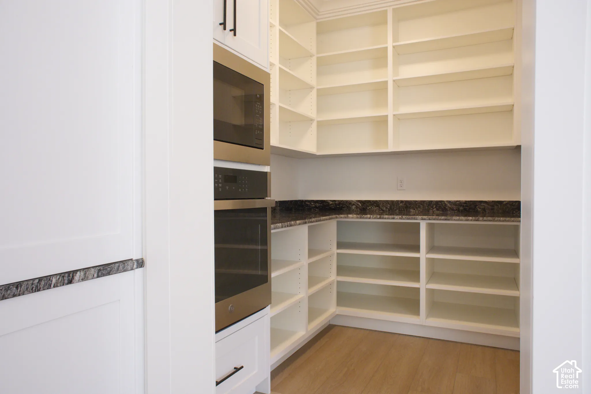 Built-in wall oven and microwave combination, extensive shelving, dark stone countertop, and wood-finish flooring