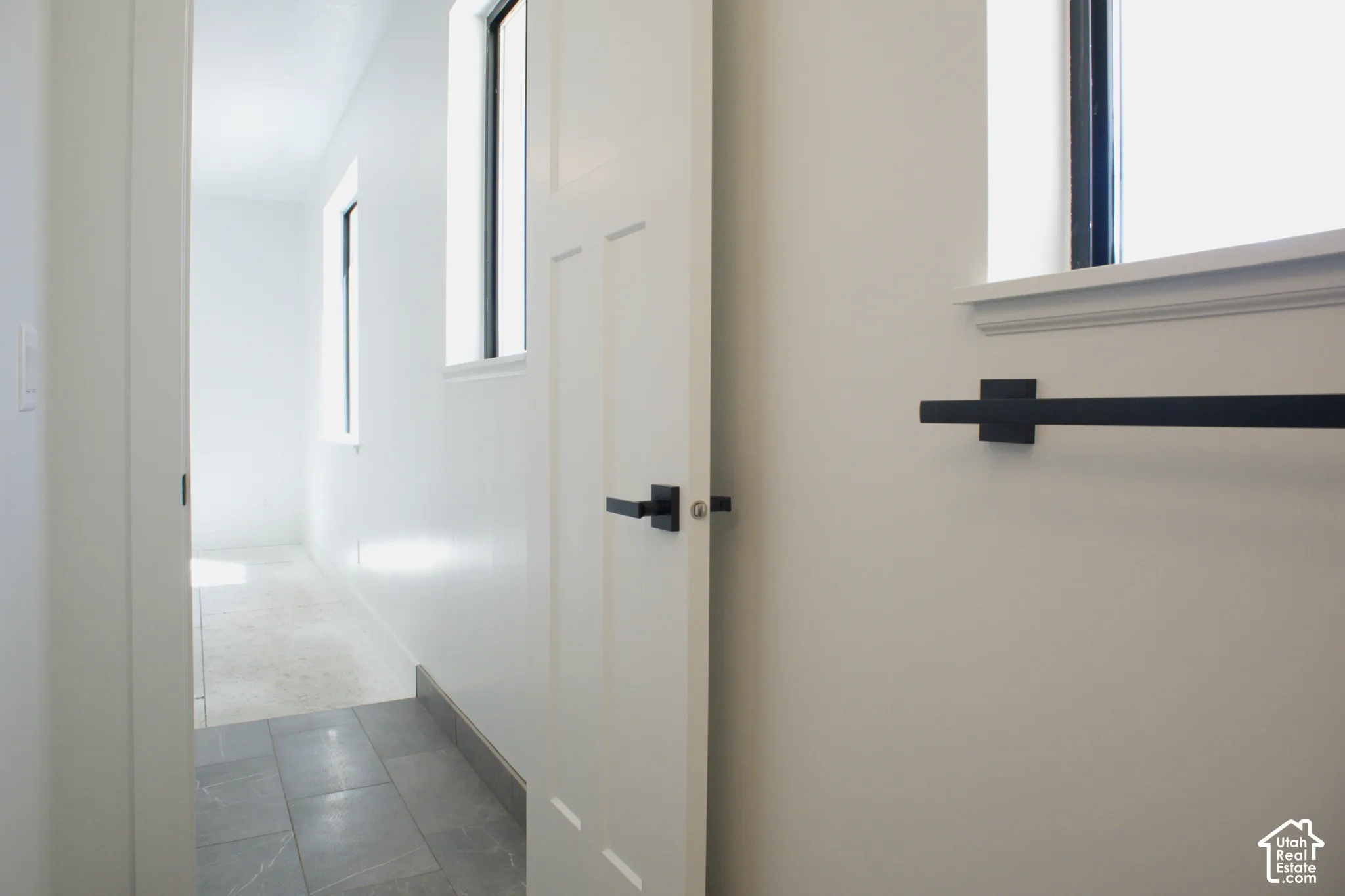 White paneled door with matte black hardware, white walls, and gray tile flooring