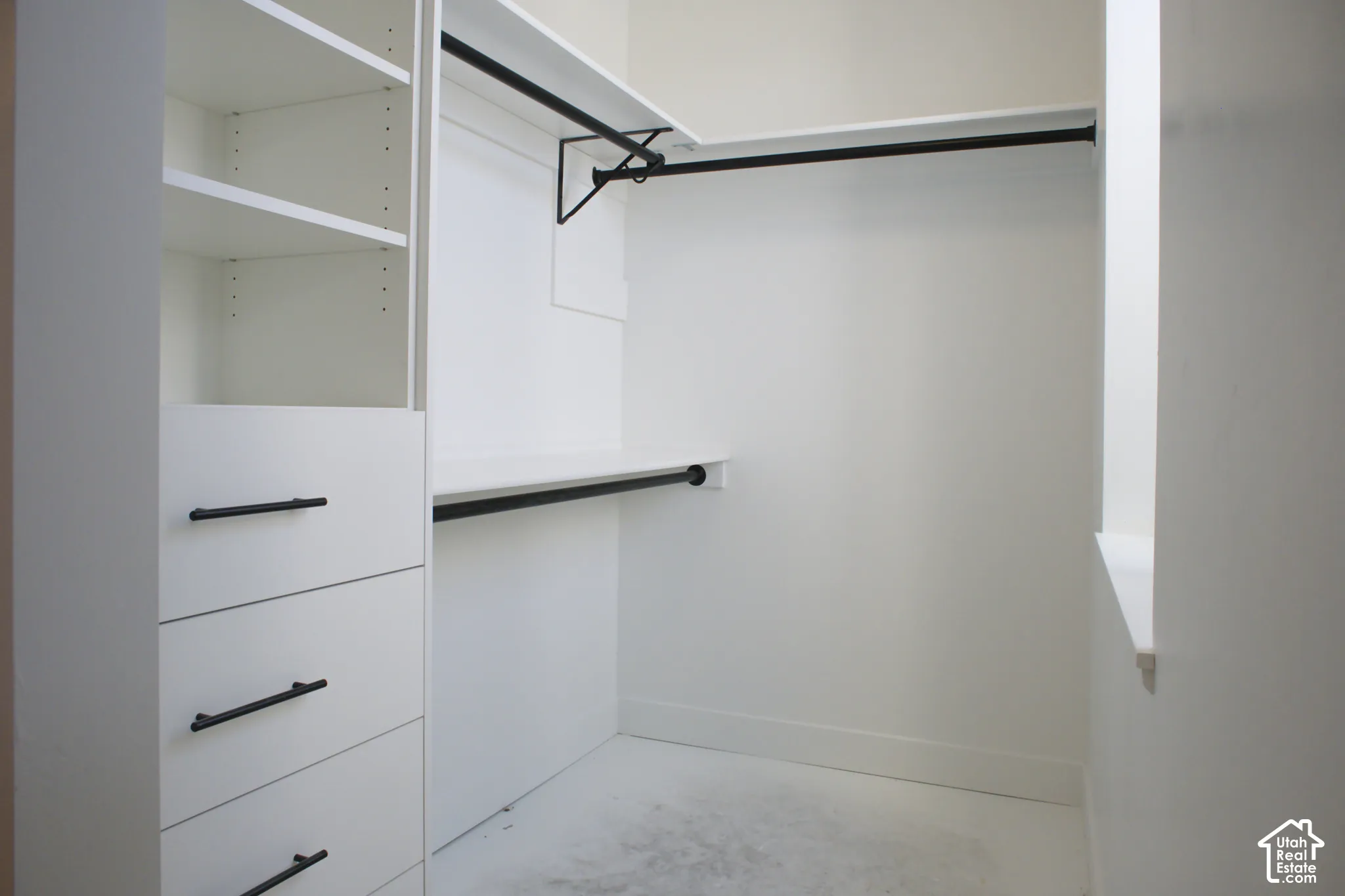 Built-in closet system featuring white shelving, multiple hanging rods, and pull-out drawers with matte black hardware