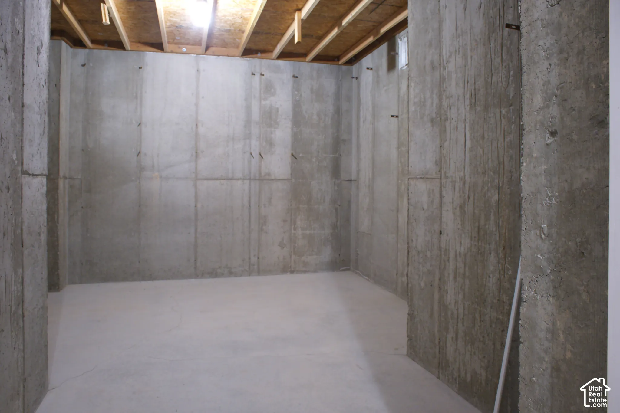 Unfinished basement space featuring concrete walls, poured concrete flooring, and exposed ceiling joists
