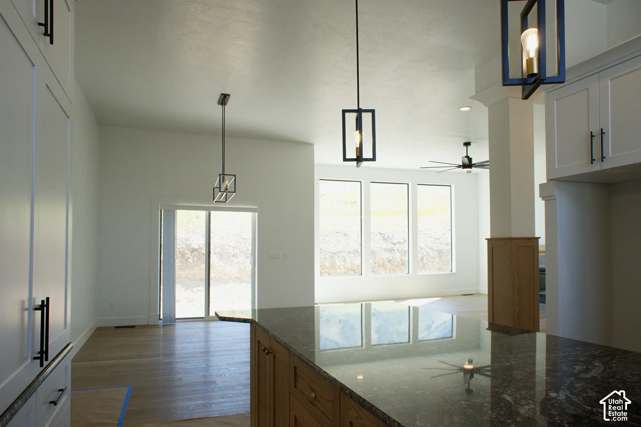 Vaulted ceiling, wood-finish flooring, full-height white cabinetry, dark granite countertop, and geometric pendant lighting