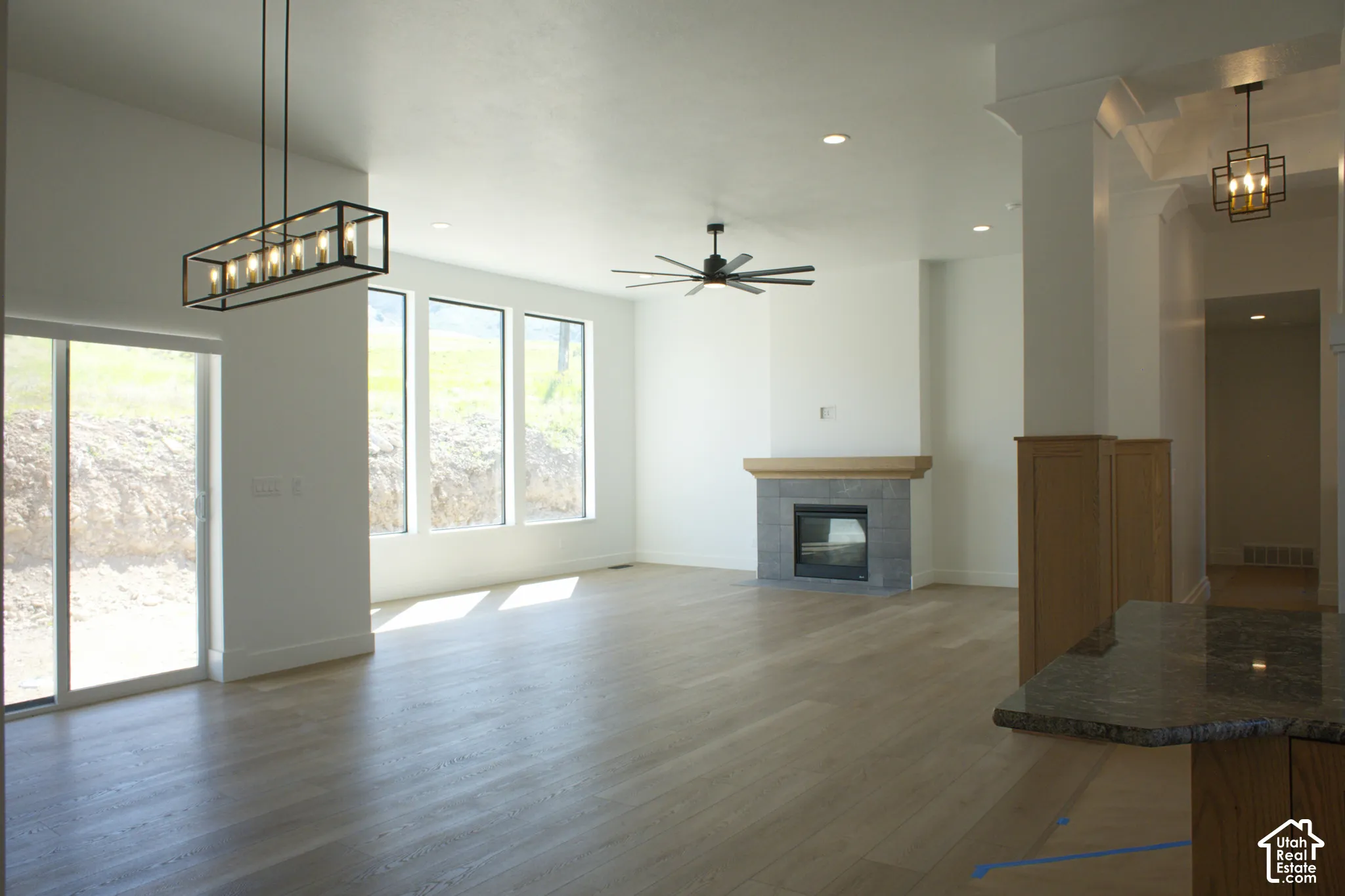 Spacious living area featuring wood-finish flooring, a fireplace with a stone surround and wood mantel, multiple large windows, and a sliding glass door