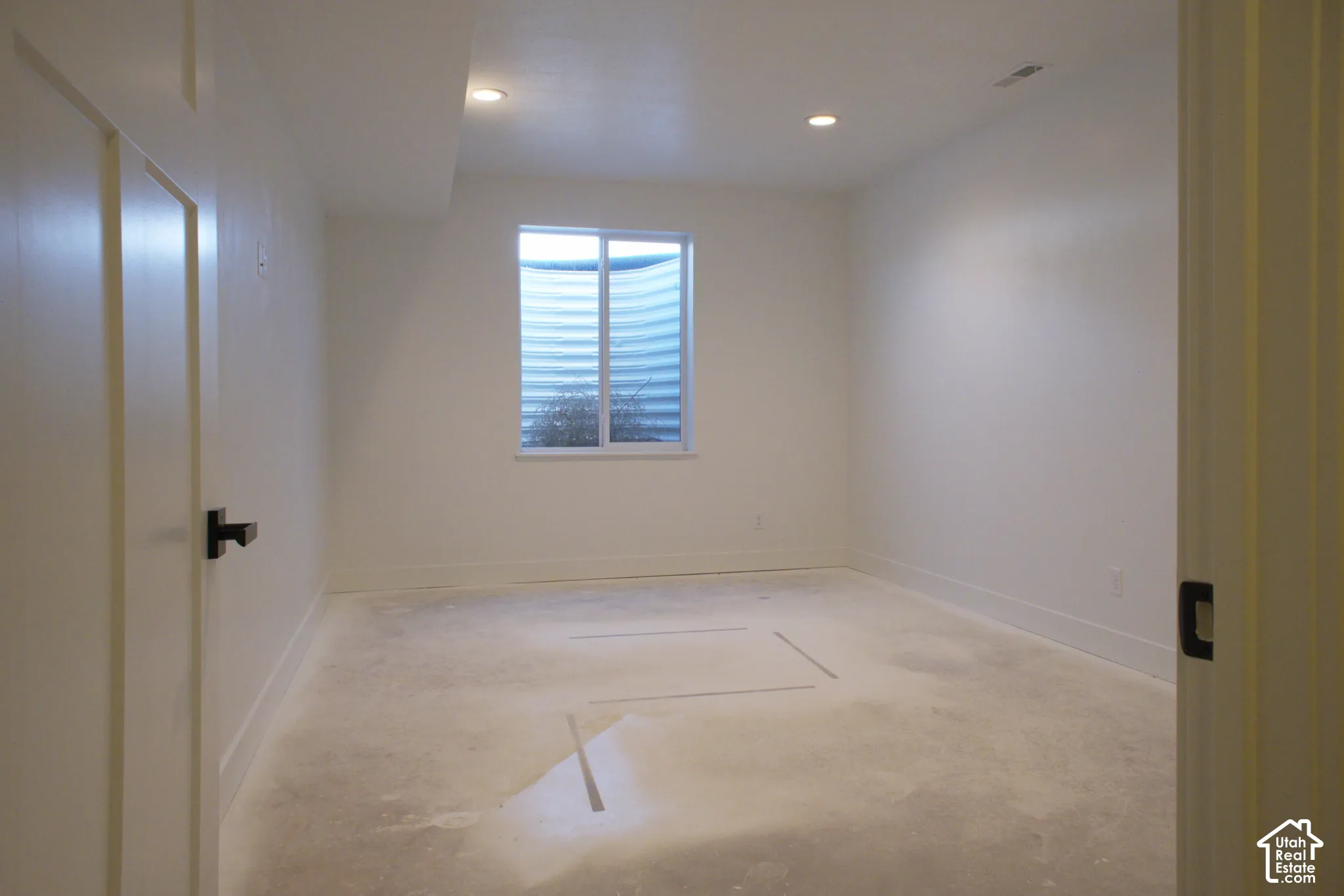 Recessed ceiling lighting, white painted walls, white trim, and a window with a window well