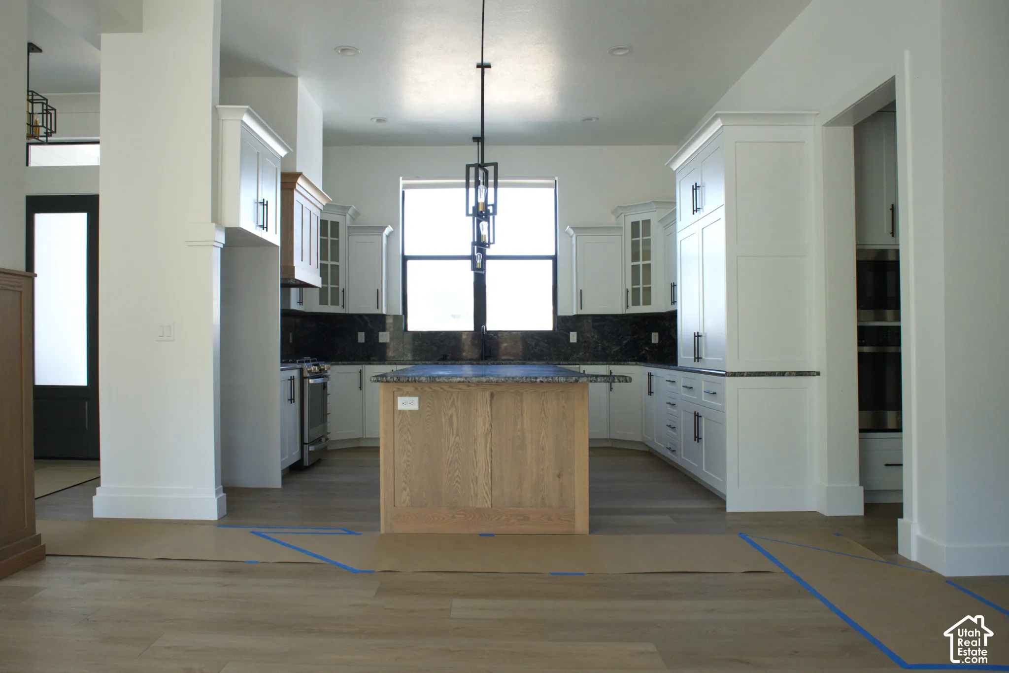 Kitchen featuring white shaker cabinetry, dark countertops, a light wood-finish island with a contrasting dark countertop, a window above the sink, and wood-finish flooring