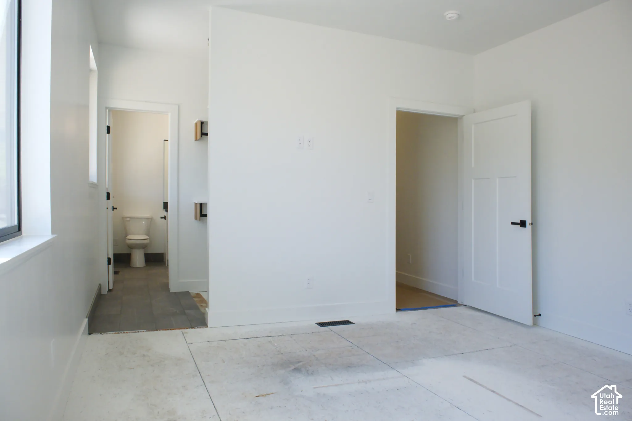 White interior walls, black-framed window, matte black door hardware, white panel door, and gray tile flooring in the adjacent space