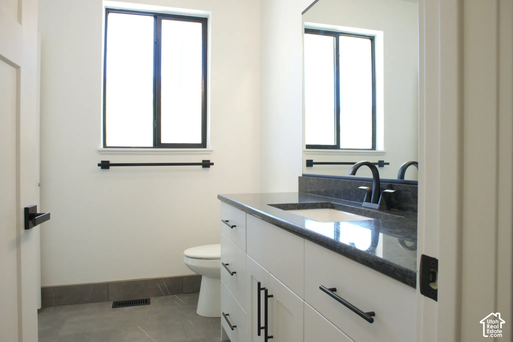 White vanity with black hardware, dark countertop, and black faucet