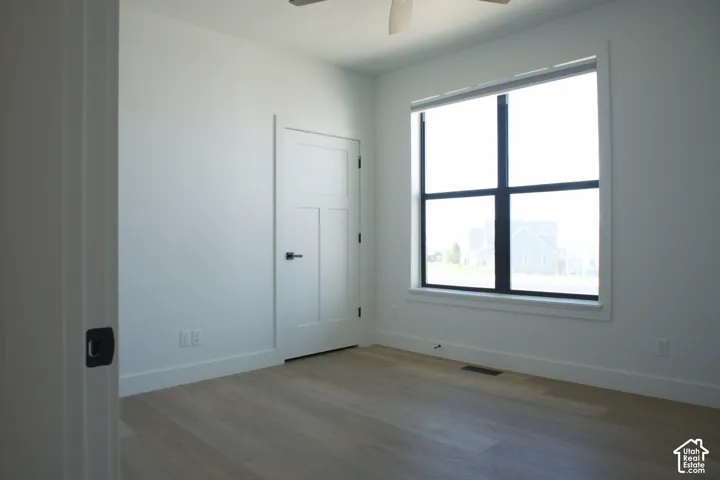 White walls and ceiling, wood-finish flooring, white solid core door with black hardware, large black-framed window, and a ceiling fan