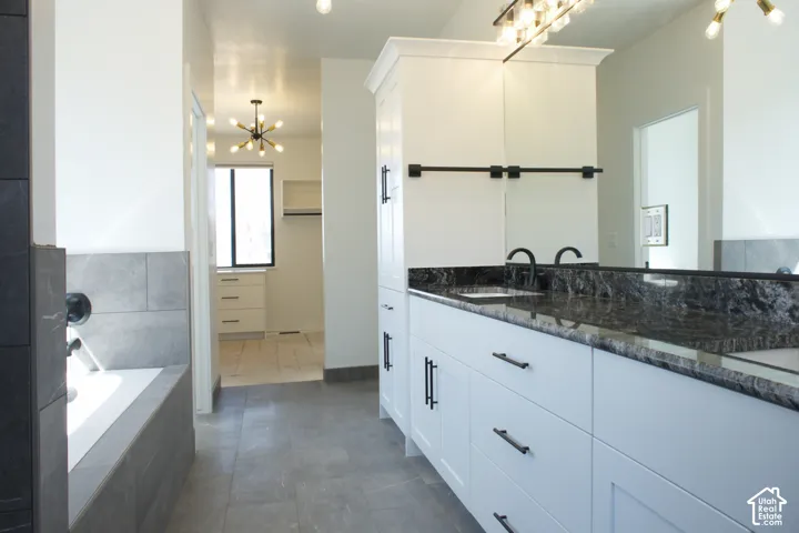 Spa-inspired primary bathroom featuring a freestanding soaking tub with tile surround, dual-sink vanity with dark stone countertops, matte black hardware, and a walk-in shower enclosed in frameless glass