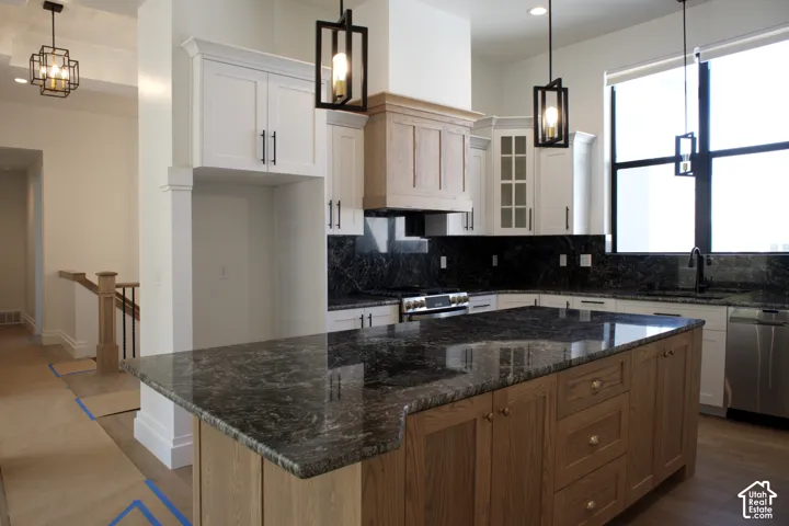 Kitchen featuring a large island with stone countertops, white cabinetry with dark hardware, a built-in oven, and pendant lighting