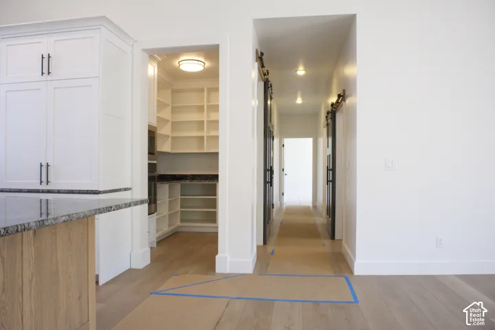 White shaker cabinetry with dark hardware, wood-finish flooring, walk-in pantry with extensive shelving, and barn doors