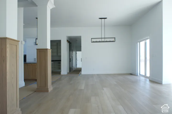 Wide plank wood-finish flooring, white walls, black linear chandelier, sliding glass door, and wood-paneled columns