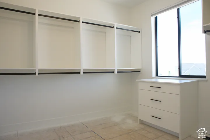 Built-in white shelving with black hanging rods, white three-drawer dresser with black pull handles, and a large window