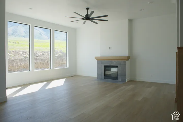 Recessed lighting, large windows, wood-finish flooring, ceiling fan, and fireplace with tile surround