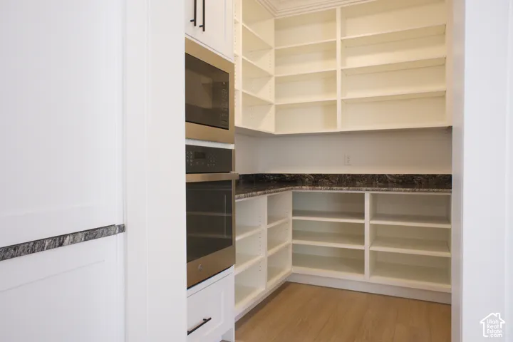 Built-in wall oven and microwave combination, extensive shelving, dark stone countertop, and wood-finish flooring