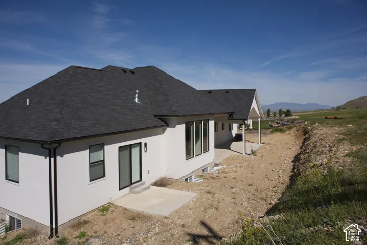 White exterior with dark roof shingles, black-framed windows, and a covered patio