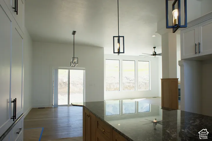 Vaulted ceiling, wood-finish flooring, full-height white cabinetry, dark granite countertop, and geometric pendant lighting