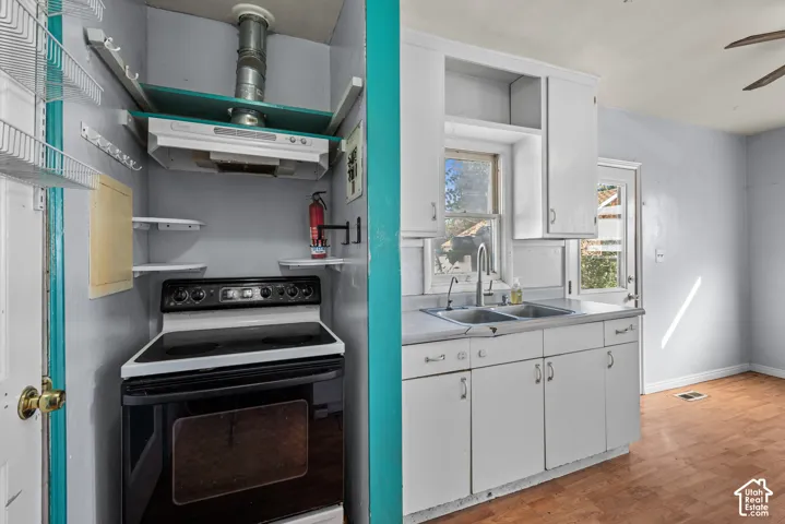 Kitchen featuring white cabinetry, wood-finish parquet flooring, stainless steel double-basin sink, and electric range with an overhead vent hood