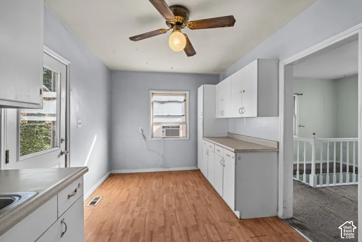 Kitchen featuring white shaker-style cabinetry, wood-finish flooring, a ceiling fan with integrated lighting, and a windowed exterior entry door