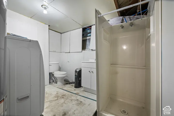 Bathroom featuring a white vanity cabinet, ceramic toilet, and pre-formed shower stall