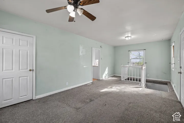 Interior space featuring a ceiling fan with integrated light fixture, neutral wall finishes, carpeting, and a white wooden balustrade