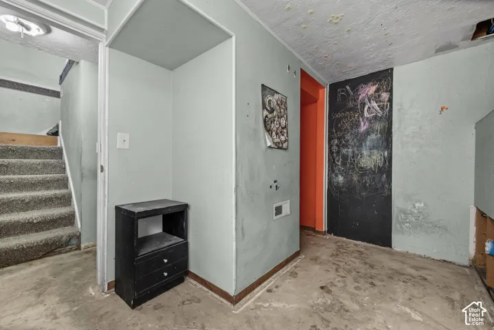 Interior space featuring concrete flooring, painted wall surfaces, and a staircase with carpeted treads