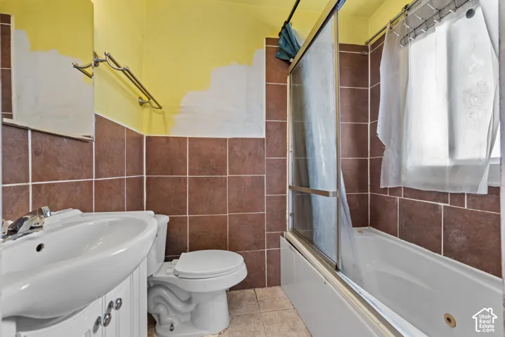 Bathroom featuring square ceramic wall tiles, a pedestal sink, and a bathtub with a glass sliding enclosure