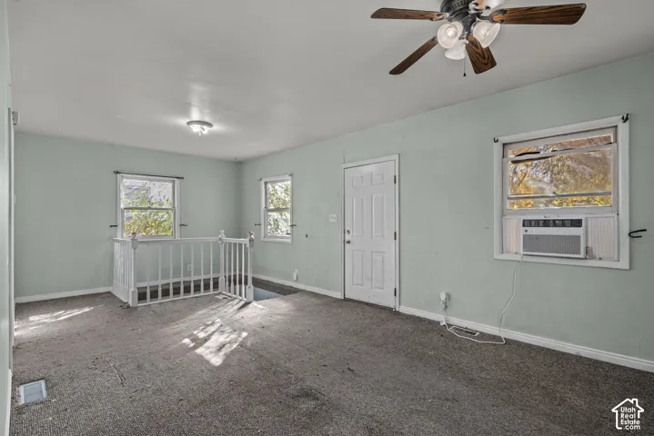 Interior space featuring wall-to-wall carpeting, a ceiling fan with integrated lighting, multiple windows, and a white wooden staircase railing