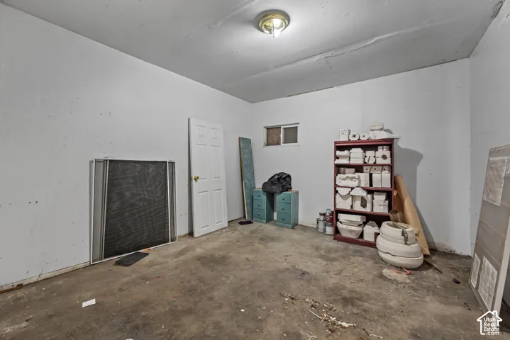 Interior room featuring a concrete floor, white walls, a flush-mount ceiling light fixture, and a single-panel interior door with a sliding window