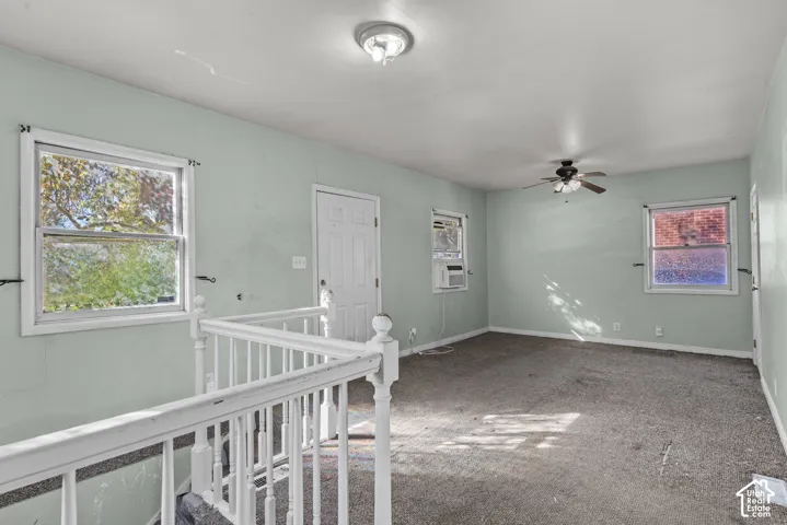 Interior room featuring wall-to-wall carpeting, multiple windows, a ceiling fan with integrated lighting, and a white balustrade railing