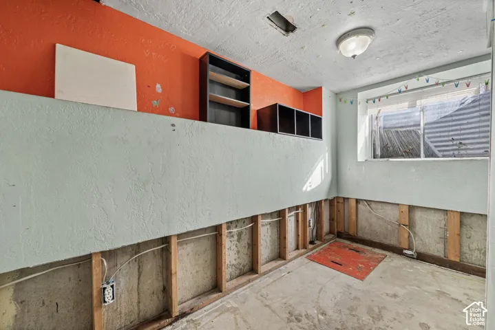 Room featuring exposed concrete foundation walls, wooden framing studs, built-in shelving units, and a window with a window well exterior