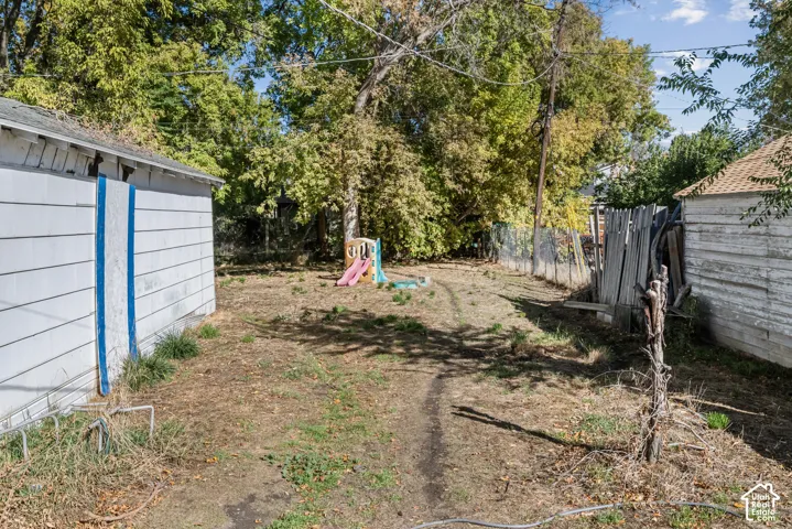 Outdoor area featuring exterior wall siding, mature trees, and wire mesh perimeter fencing
