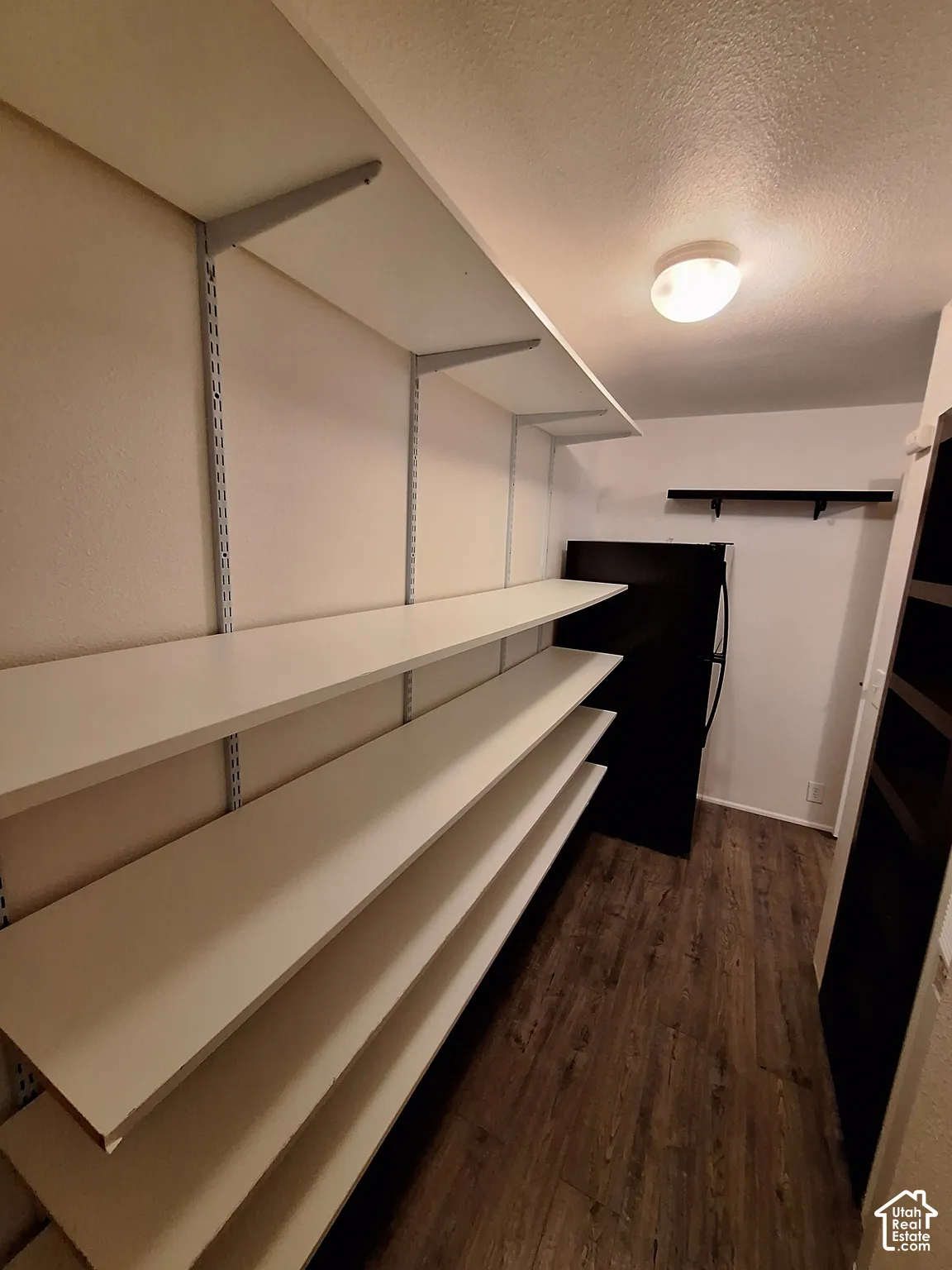 Adjustable wall-mounted shelving, wood-finish flooring, recessed ceiling lighting, and a dark-finish refrigerator