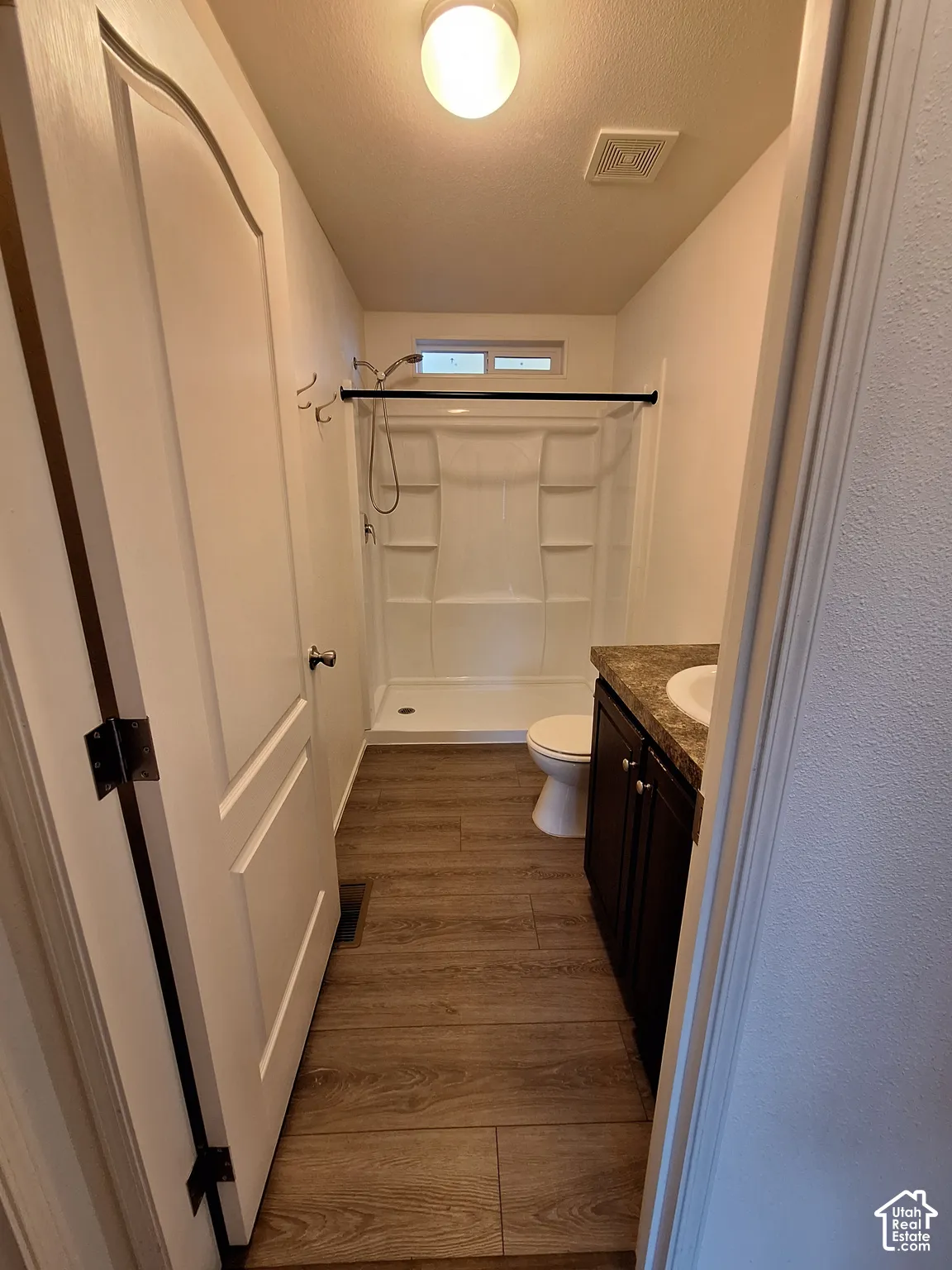 Bathroom featuring wood-finish flooring, a white vanity sink with a dark countertop, and a shower with a built-in shelf