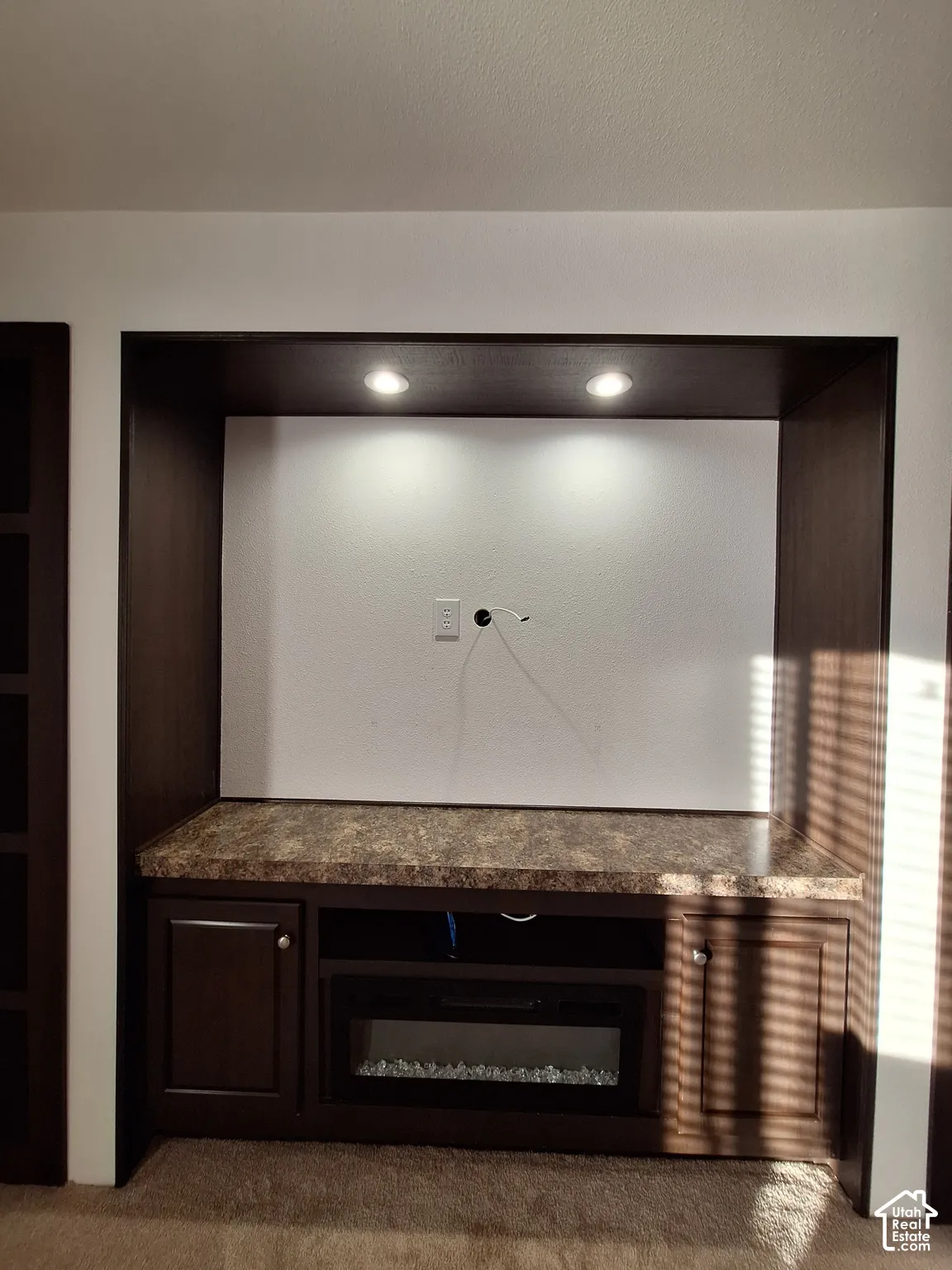 Built-in entertainment center featuring recessed lighting, a stone-finish countertop, dark wood-finish cabinetry, and an integrated electric fireplace