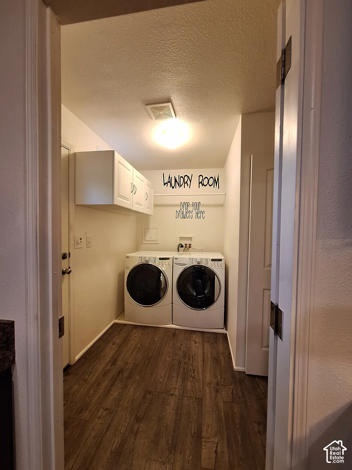 Dedicated laundry area featuring wood-finish flooring, white wall cabinets, and an overhead light fixture