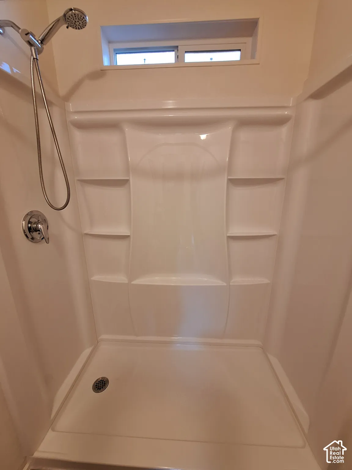 Spacious shower enclosure featuring a seamless acrylic surround with built-in shelving, chrome showerhead with handheld attachment, and a slip-resistant floor with integrated drain