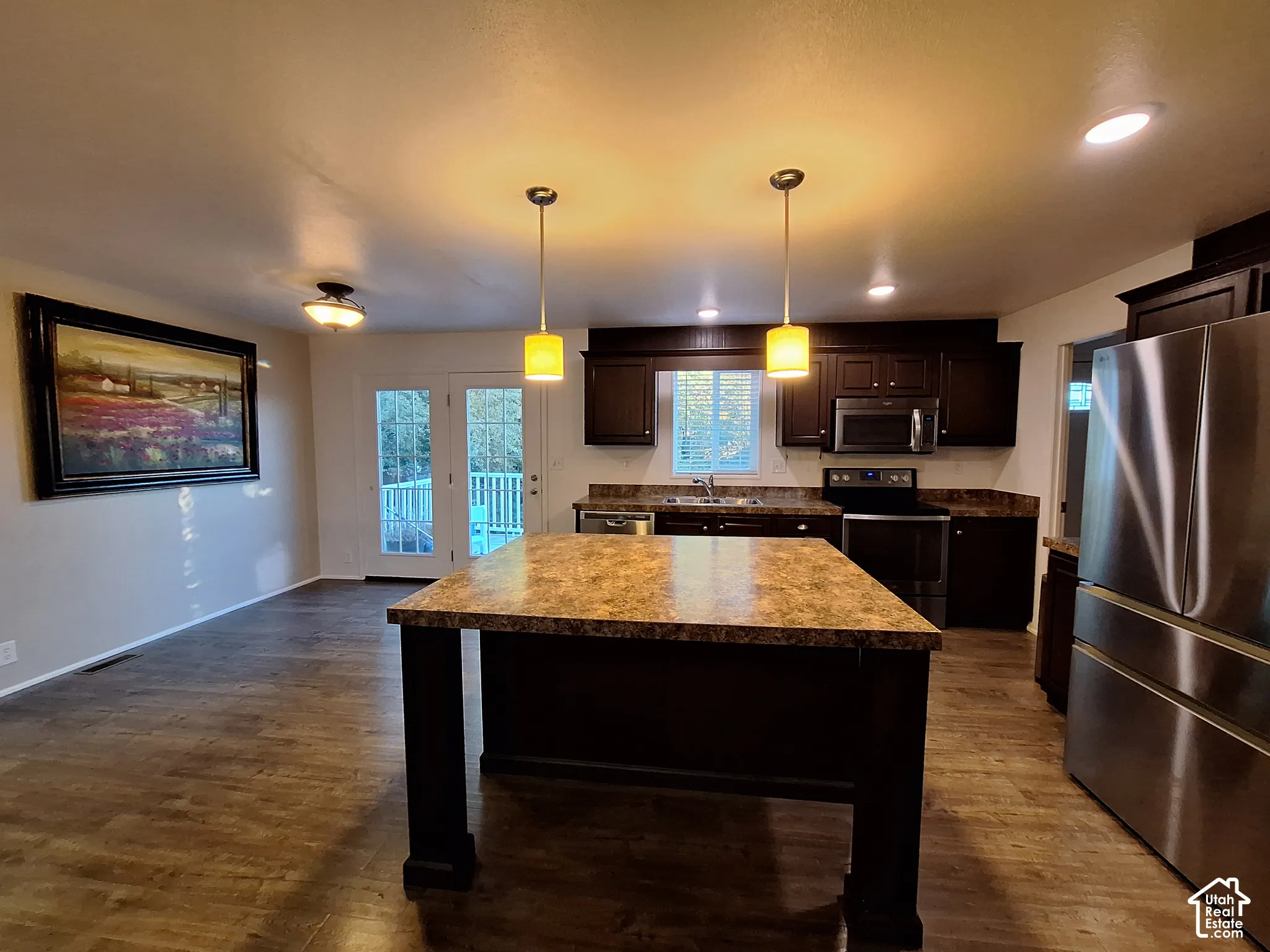 Central kitchen island with a stone-finish countertop, dark wood-finish cabinetry, stainless steel appliances, and wood-finish flooring