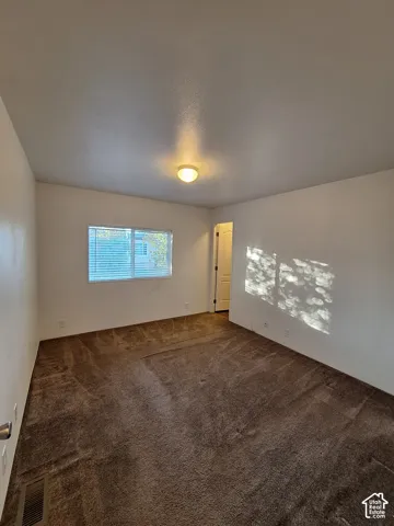 White walls, brown carpet flooring, and a single window with blinds