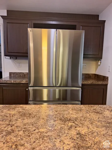 Stainless steel French door refrigerator, dark wood-finish cabinetry, and patterned countertops